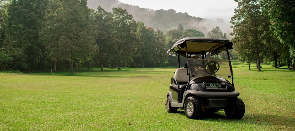 Ein Golfcart steht auf einem weitläufigen Golfplatz, umgeben von hohen Bäumen und sanftem Morgennebel. Die Szene vermittelt die ruhige Atmosphäre eines modernen Golfplatzes inmitten der Natur.