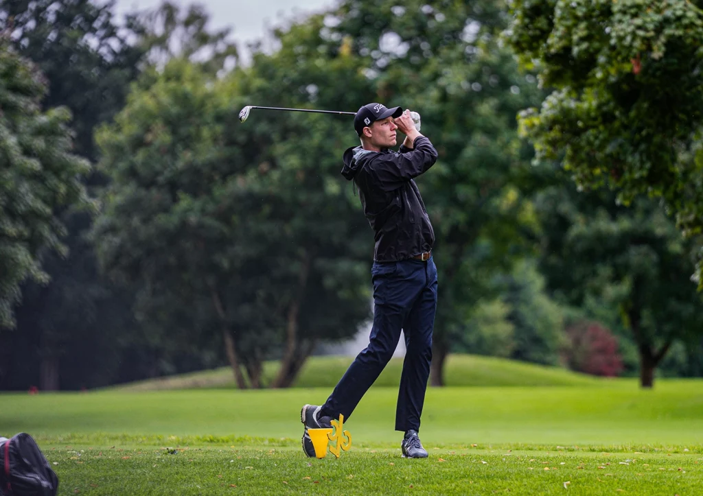 Golfer beim Abschlag auf dem Fairway vor bewaldeter Kulisse