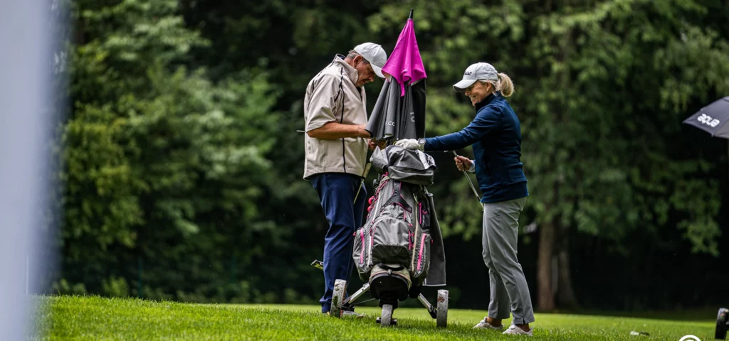 Zwei Golfer stehen am Bag. Sie sprechen und lächeln.