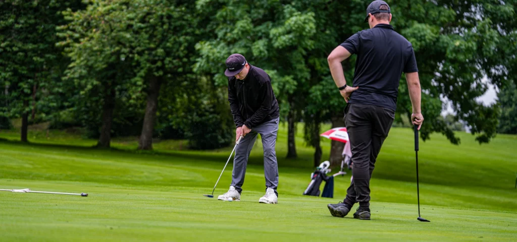 Golfer bereitet sich auf einen Putt vor. Ein Mitspieler steht daneben und schaut zu.